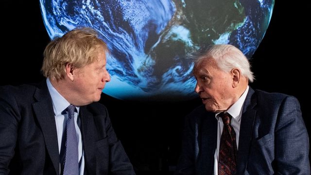 Boris Johnson and David Attenborough talking in front of a projection of Earth