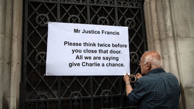 Человек прикрепляет плакат в поддержку Чарли Гарда на дверь суда