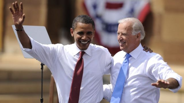 Barack Obama and Joe Biden wave while arm-in-arm.