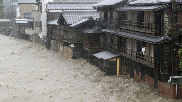 Men watch from their balcony as a river floods their home in Ise