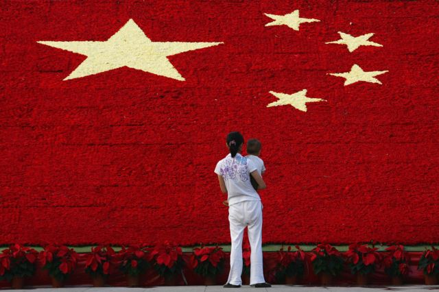 A woman holds her son as she looks at the national flag made up of 100,000 carnations at Wuling Square 25 September 2007 in Hangzhou, China.