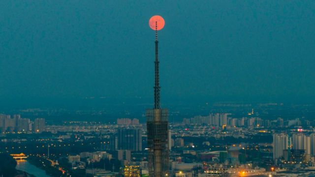 Çin'in Huai'an şehrinde, televizyon kulesinin ardından kızıl rengiyle parlayan dolunay.