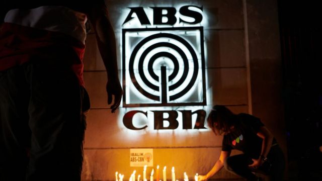 : Employees and supporters of ABS-CBN light candles in front of its main studio to show support