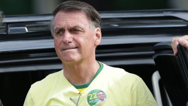 Bolsonaro, um homem idoso de cabelo castanho e branco, faz feição de preocupado em frente a um carro preto