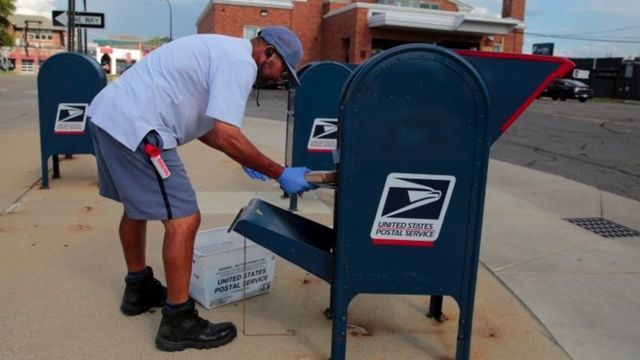 A postman takes letters out of a mailbox.