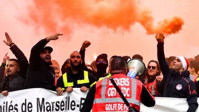 Des dockers marchent avec des bombes fumigènes et tiennent une banderole lors d'une manifestation pour protester contre les révisions des retraites, à Marseille, dans le sud de la France, le 5 décembre