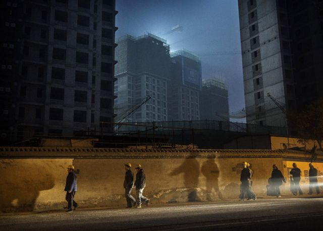 Workers in Beijing walk past an apartment building under construction after get off work at night (file photo)