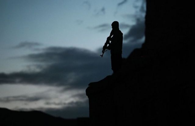 A policeman holding a gun silhouetted against a darkening sky