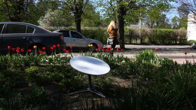Una persona mira un teléfono inteligente cerca de una terminal de internet SpaceX Starlink instalada en un jardín de flores el 5 de mayo de 2022 en Vorzel, Ucrania.