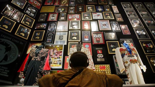 Una persona ve a una pared llena de memorabilia de elvis, discos, discos de oro y trajes.