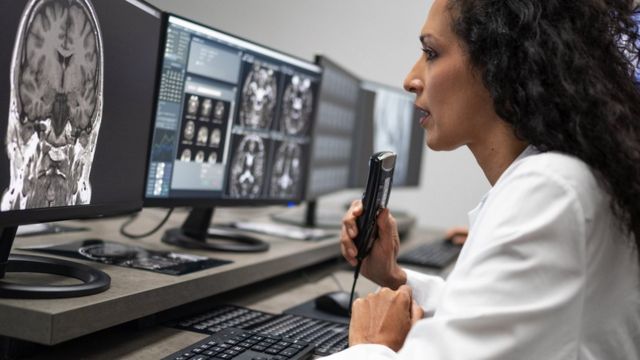 Uma pesquisadora olhando para uma tomografia do cérebro no computador e falando em um ditafone