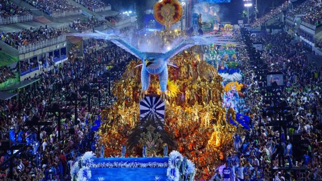Águia azul gigante à frente de foliões com fantasias douradas no sambódromo do Rio