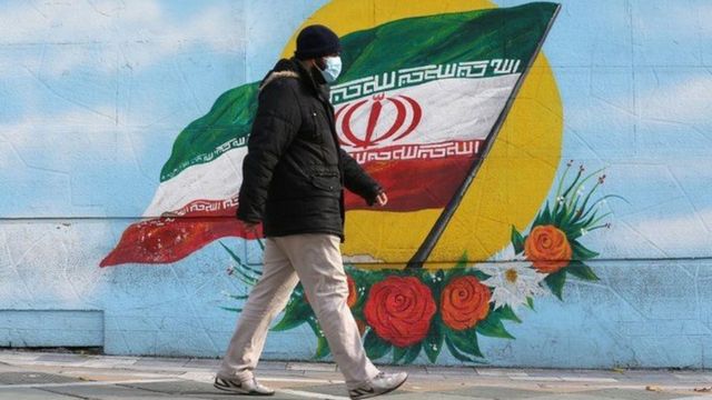 شخص يرتدي كمامة يسير حذاء جدار مرسوم عليه العلم الإيراني