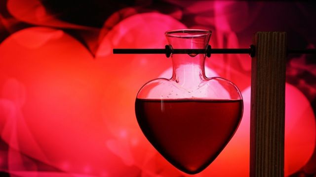 Tubo de laboratorio en forma de corazón en fondo rojo