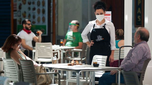 Garçonete de máscara em restaurante