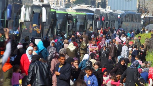 الذين تم إجلاؤهم من كفريا والفوعة يقفون قرب الحافلات التي ستقلهم إلى حلب