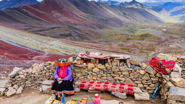 Mujer andina sentada de espaldas a la Montaña de los Siete Colores.