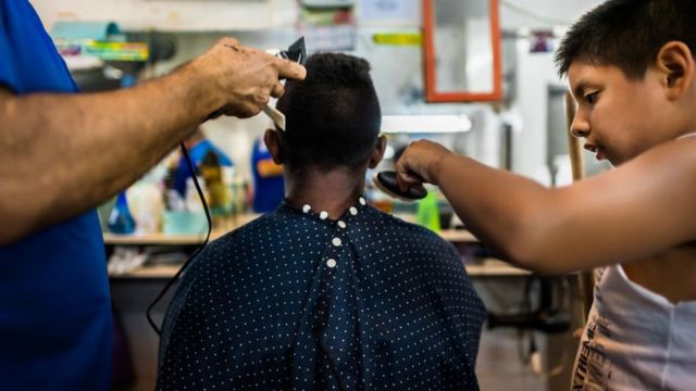 Barbeiro corta o cabelo de um menino na favela da Rocinha, Rio de Janeiro
