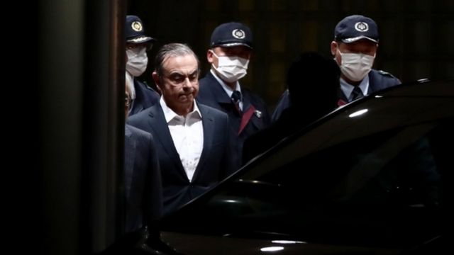 Carlos Ghosn is escorted as he walks out of the Tokyo Detention House following his release on bail in Tokyo in April 2019
