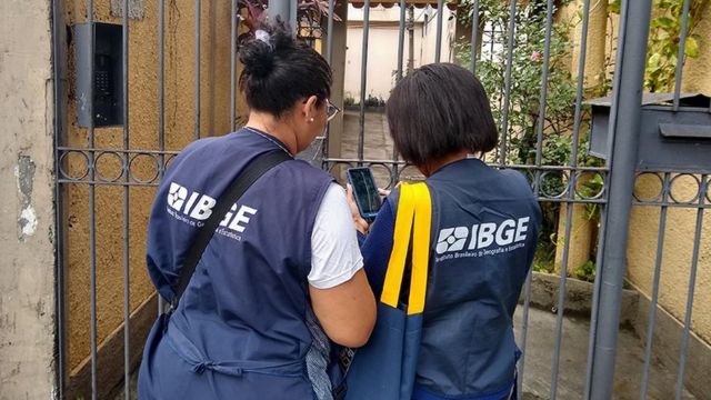 Recenseadoras usando colete do IBGE em frente ao portão de um domicílio