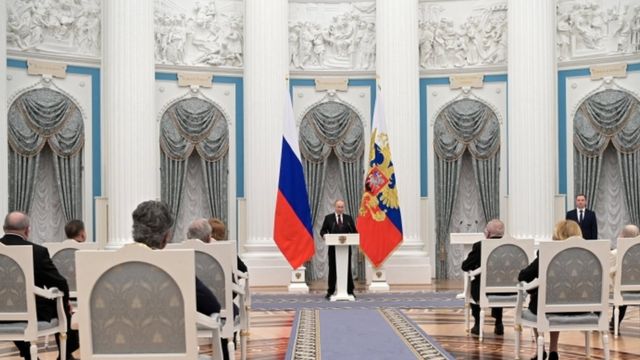 Putin discursa em salão no Kremlin, observado por pessoas que aparecem de costas, em cadeiras na plateia
