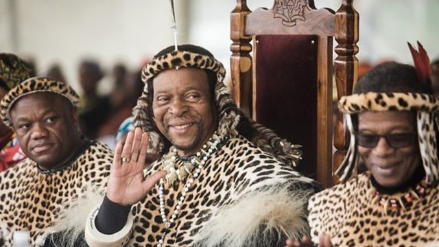 Rei Zwelithini acena em uma cerimônia, sentado e vestido com roupas tradicionais