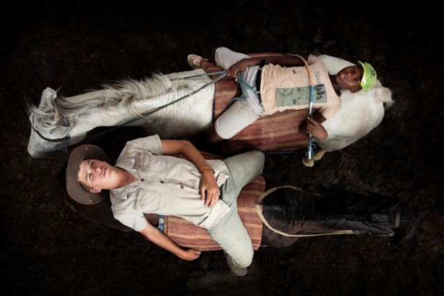 Aerial view of two young people lying on the backs of horses