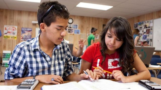 Dois adolescentes sentados lado a lado escrevem em uma caderno