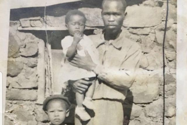 A photo of Agnes Sithole with her younger sister and father outside the house she was born in