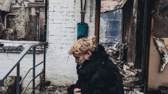 Una mujer camina frente a una casa destruida en Irpín