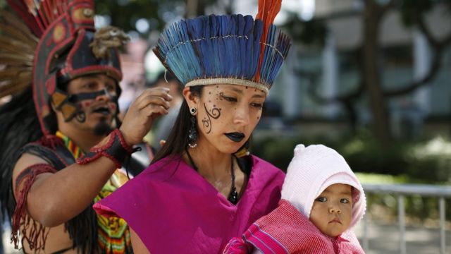 Woman holds baby as she is helped into her costume for start of Day of the Dead parade along Mexico City's main Reforma Avenue, Saturday, Oct 29, 2016