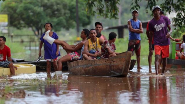 Several people use a canoe to navigate a flooded area in Brazil