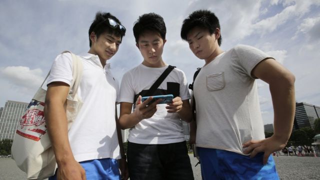 皇居の近くで、携帯端末を使い天皇陛下のお言葉を見る若者たち。