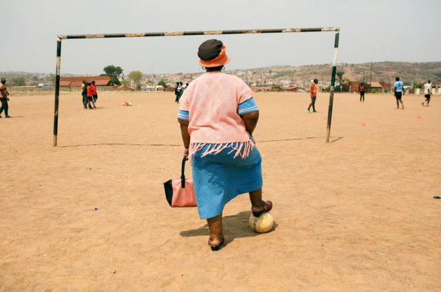 A woman stands on a sandy football pitch