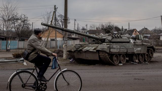 Um homem passa de bicicleta por um tanque russo destruído em 30 de março de 2022 em Trostyanets, Ucrânia