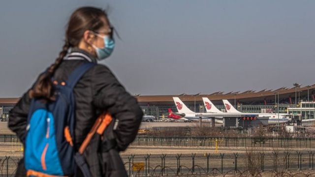 Mulher chinesa de máscara diante de aviões em Pequim