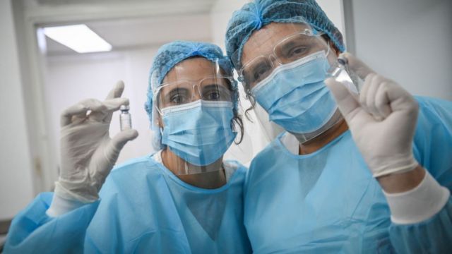 Dois profissionais de saúde exibem vidro com vacina