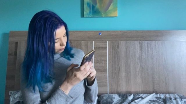 Sex worker Estelle Lucas sits on her bed looking at her smartphone