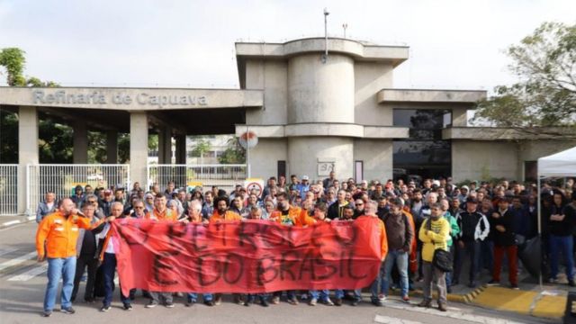 Petroleiros parados em frente à Refinaria de Capuava, com uma faixa vermelha onde se lê "O Petróleo É do Brasil"