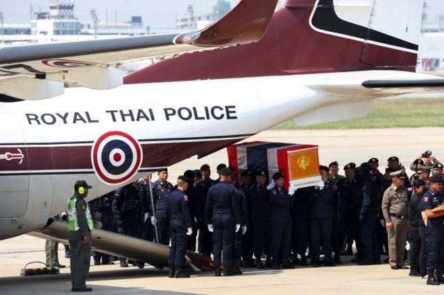 คนกำลังแบกโลงศพที่ถูกคลุมด้วยธงชาติฉากหลังเป็นเครื่องบินของตำรวจ