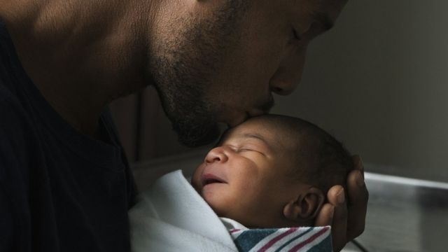 A man kisses the forehead of a newborn baby