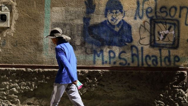 Una persona camina frente a una pared con una imagen de Evo Morales