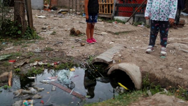 Pés de crianças perto de esgoto a céu aberto em Laferrere, na periferia de Buenos Aires