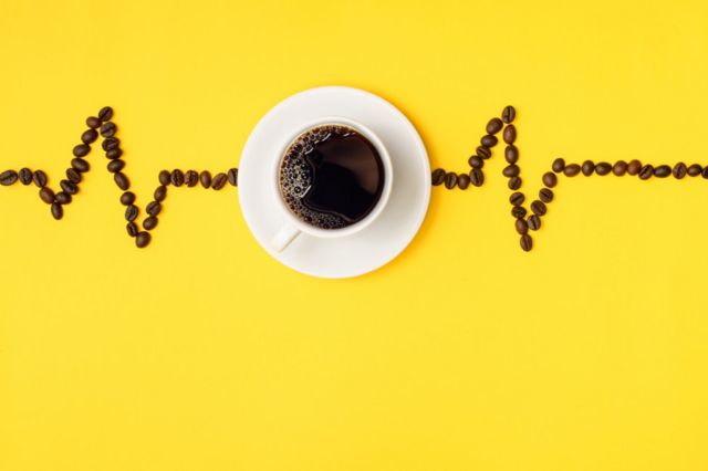 Uma xícara de café com grãos de café em volta simulando uma frequência cardíaca