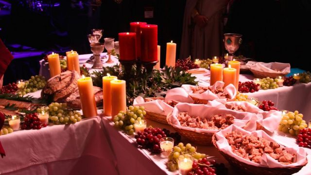 Красные и белые свечи в центре стола, разложенные кисти винограда и множество тарелок с мясом