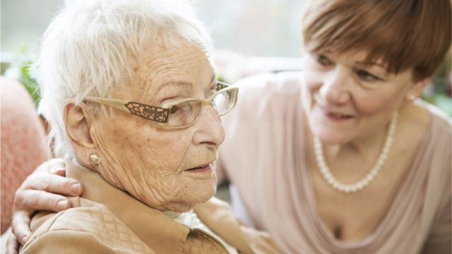 An elderly woman together with another middle-aged woman.