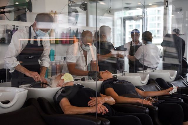 Women lean back to have their hair washed with plastic barriers dividing each customer