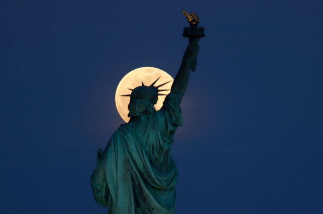 The Statue of Liberty in New York City, US, seen with the rising supermoon in the sky