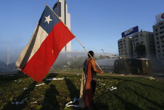 A man holds a Chilean flag in front of a tank