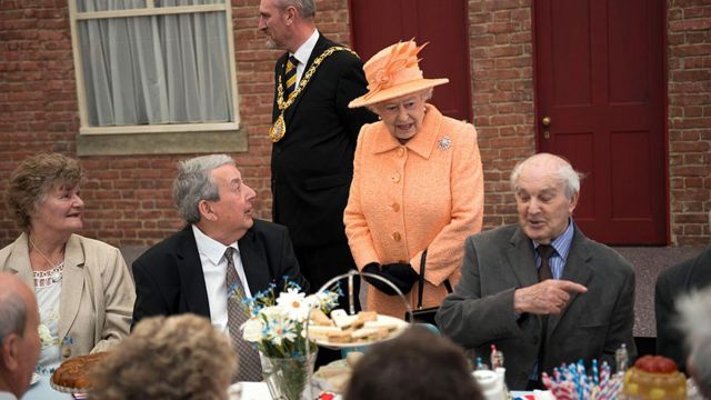 The Queen speaks to people sat at a table for a Jubilee street party in 2012